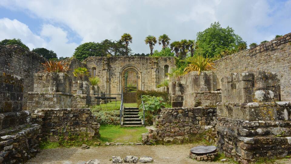 An ancient stone structure with a central arched doorway, surrounded by lush greenery and palm trees.