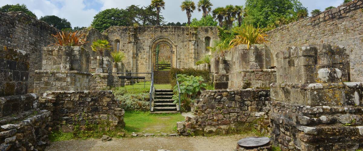 An ancient stone structure with a central arched doorway, surrounded by lush greenery and palm trees.