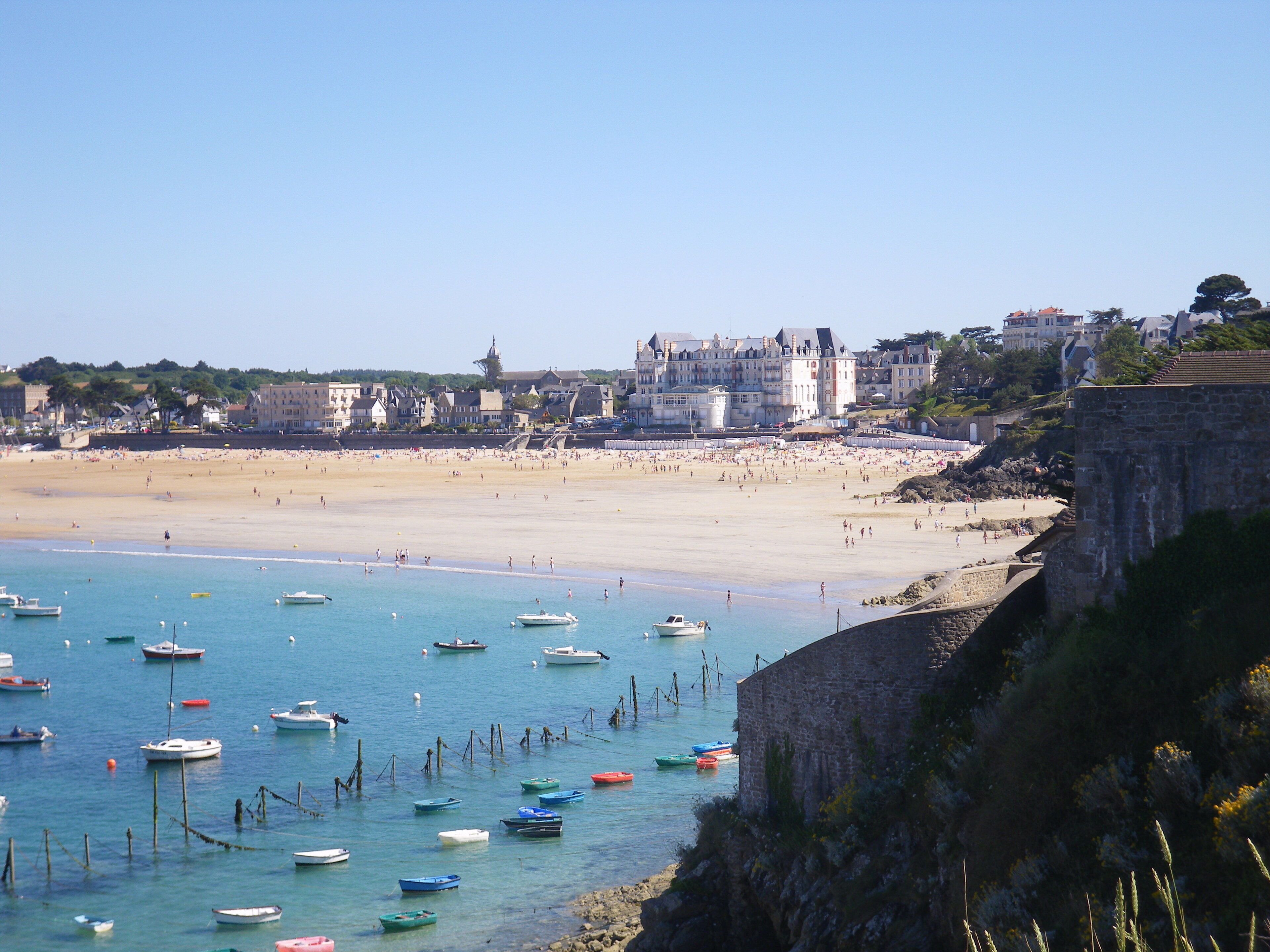 A coastal town with a sandy beach, numerous boats, and historic buildings.
