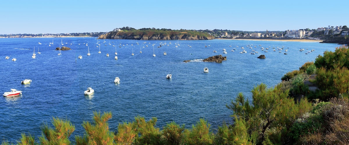 A coastal town with numerous boats on the water, rocky outcrops, and a clear blue sky.