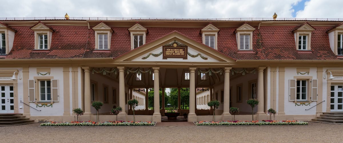 A grand building with a red-tiled roof, a central entrance with columns, and a sign above it.