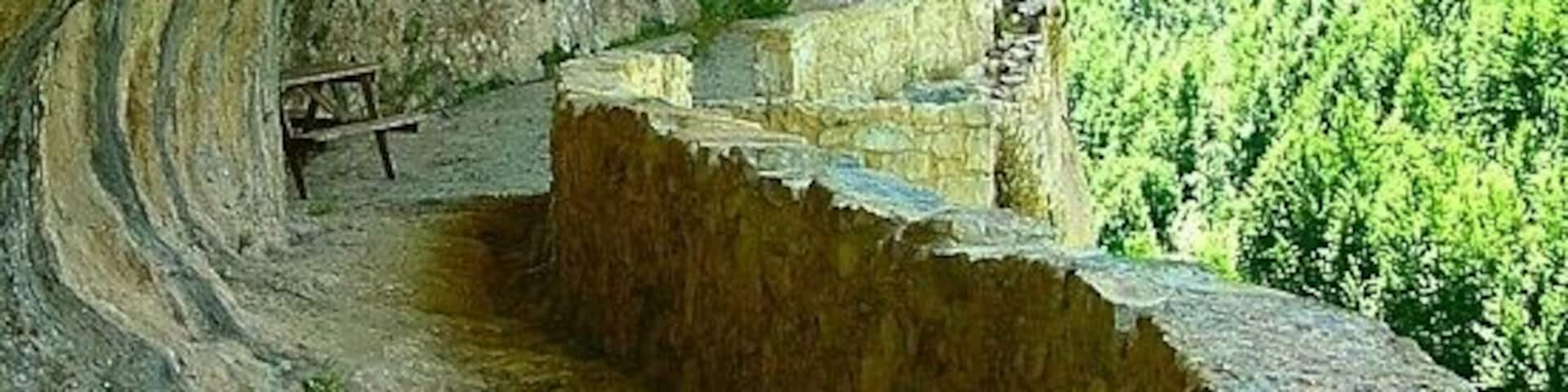 A stone pathway leading to a building carved into a cliffside, overlooking a forested valley.