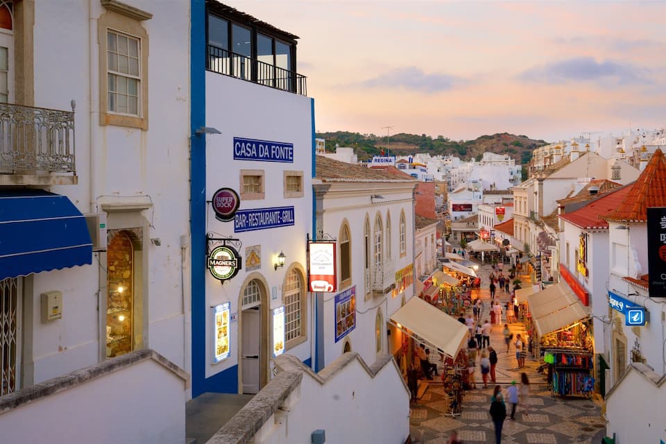 A bustling street in a historic town with white buildings, shops, and signs for restaurants and bars.