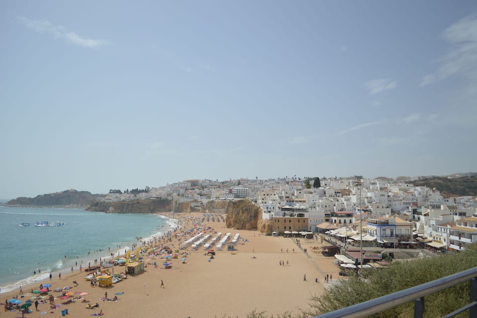A coastal town with a sandy beach, umbrellas, and buildings along the shore.