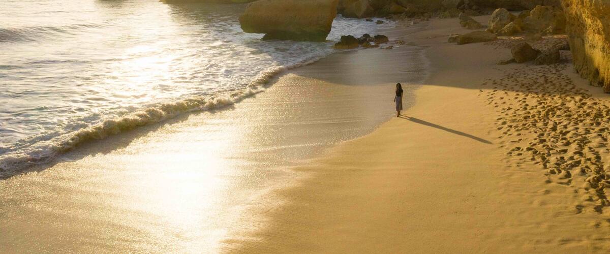 A beach with large rock formations and a person standing on the sand.