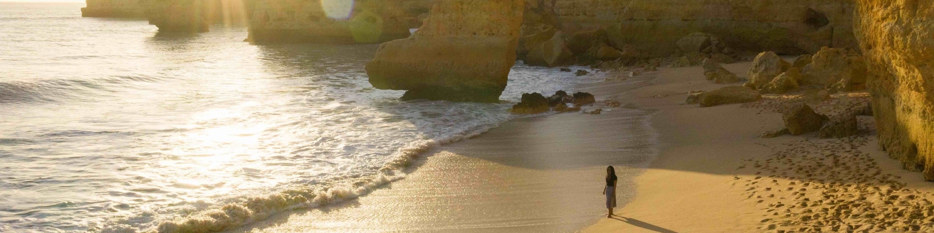 A beach with large rock formations and a person standing on the sand.
