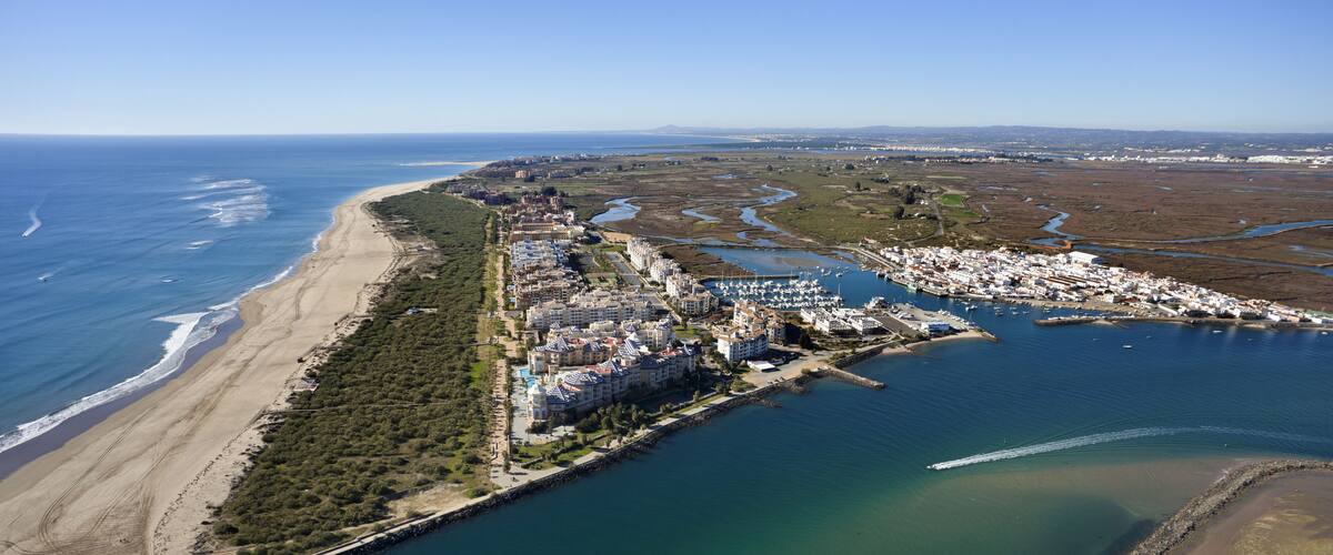 An aerial view of a coastal town with a beach, marina, and residential buildings.