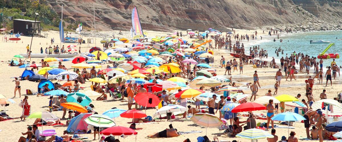 A crowded beach with numerous colorful umbrellas and people relaxing on the sand.