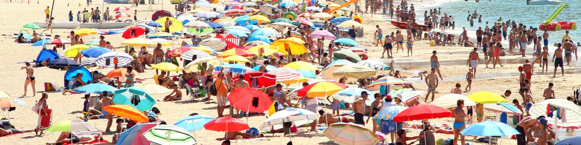 A crowded beach with numerous colorful umbrellas and people relaxing on the sand.