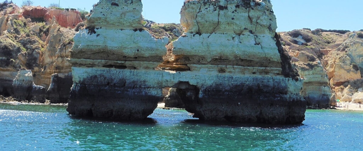 Une formation rocheuse côtière surmontée d’une arche naturelle qui s’étend au-dessus d’eaux turquoise.
