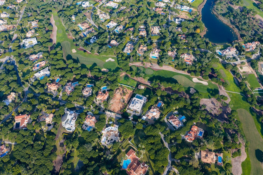 An aerial view of a residential area with houses, golf courses, and a lake.