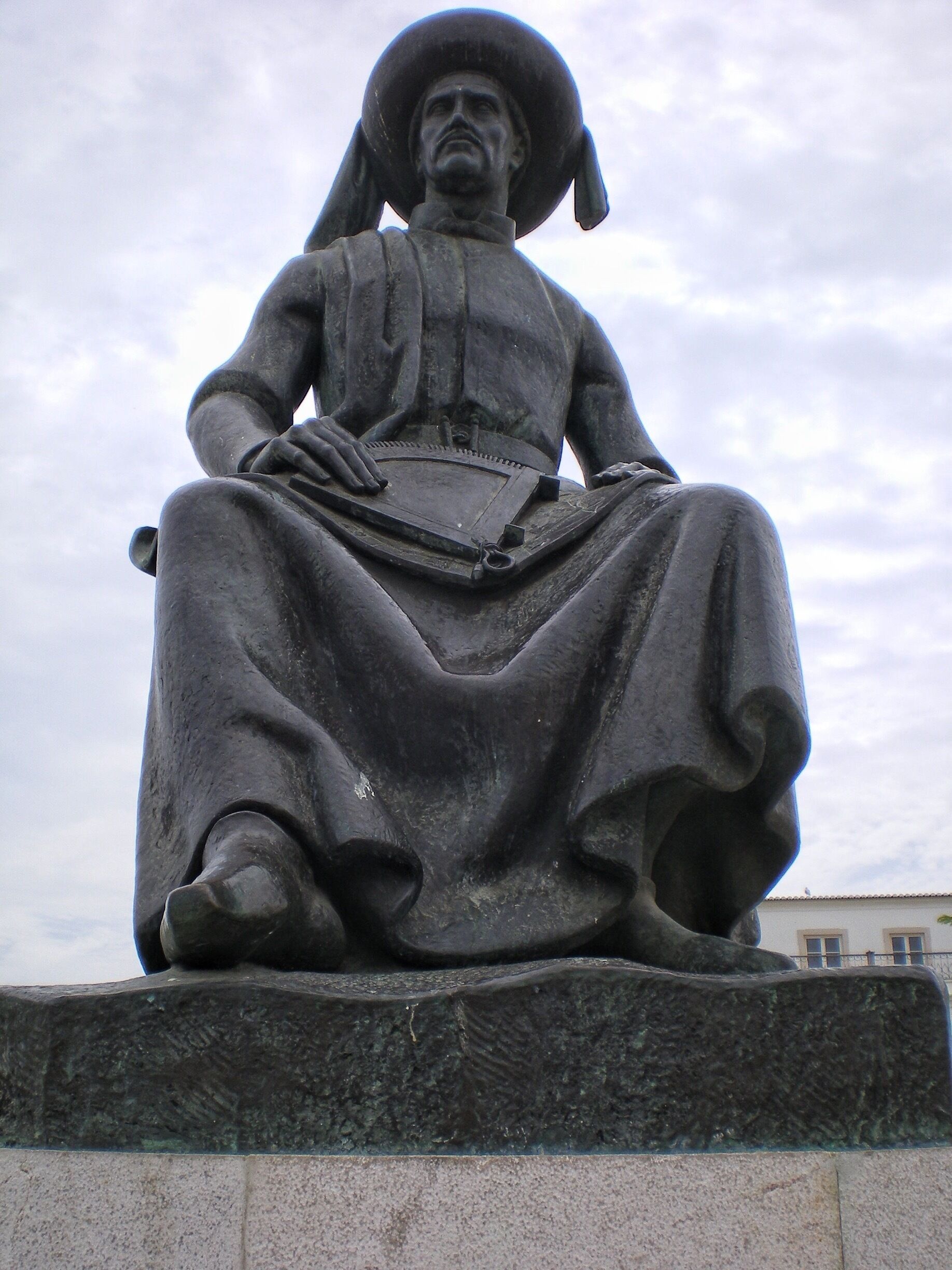 A statue of a seated figure with a large hat and a long skirt.