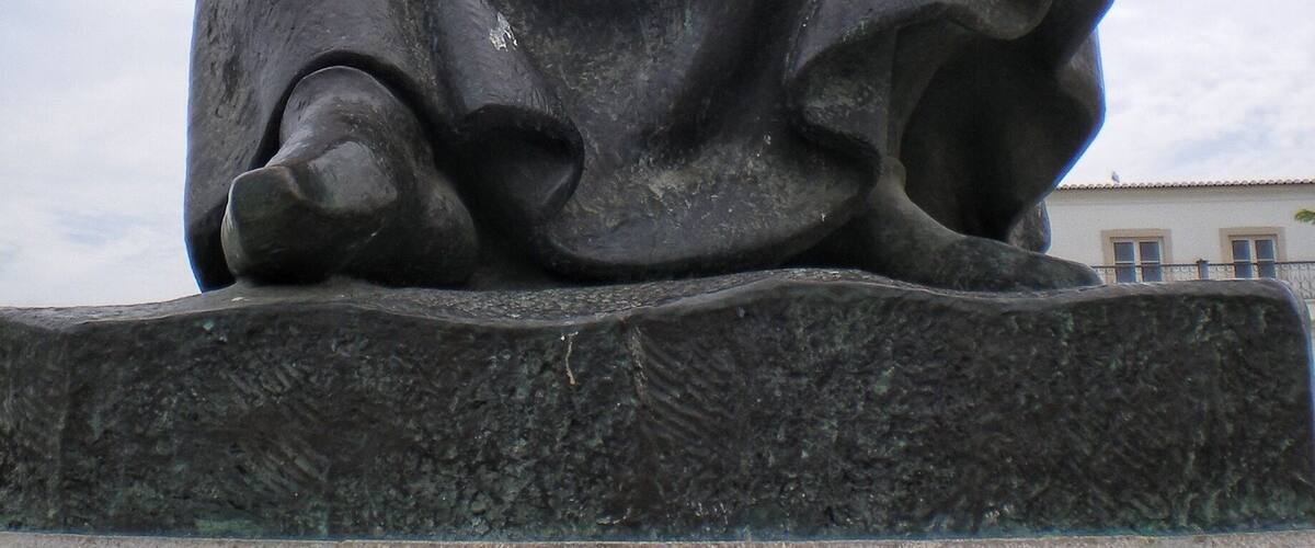 A statue of a seated figure with a large hat and a long skirt.