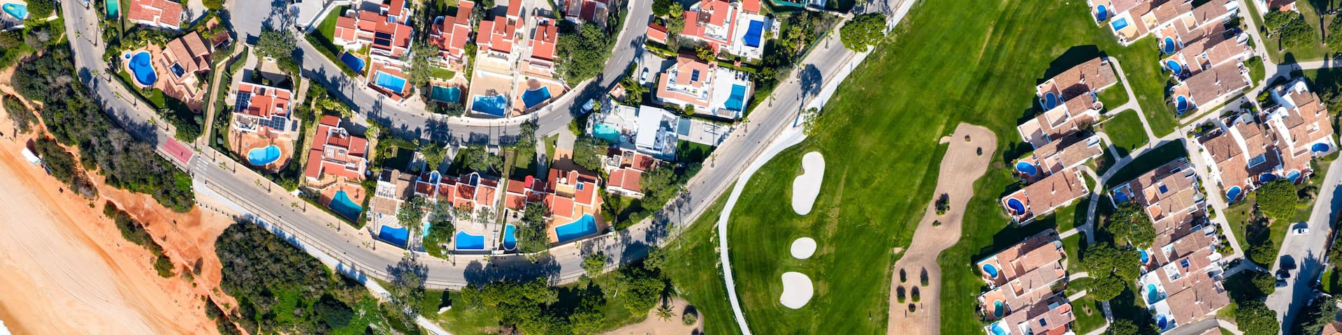 An aerial view of a coastal residential area with beachfront properties, a golf course, and a well-maintained park.