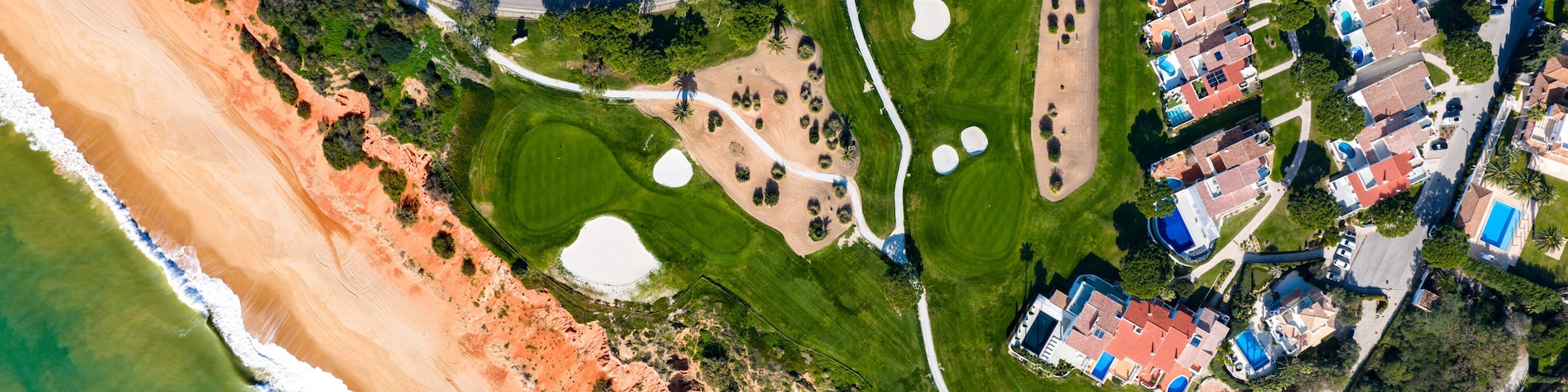 Vista aérea de una zona residencial costera con propiedades frente al mar, un campo de golf y un parque bien cuidado.
