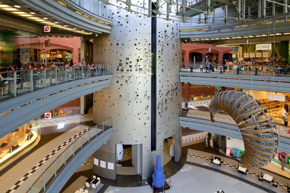 A multi-level shopping mall with a central spiral staircase, various retail stores, and a prominent blue sculpture.