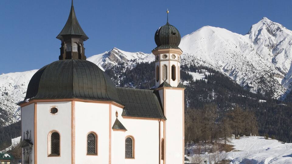 A snow-covered church with a dome and bell tower, surrounded by snow-covered mountains.