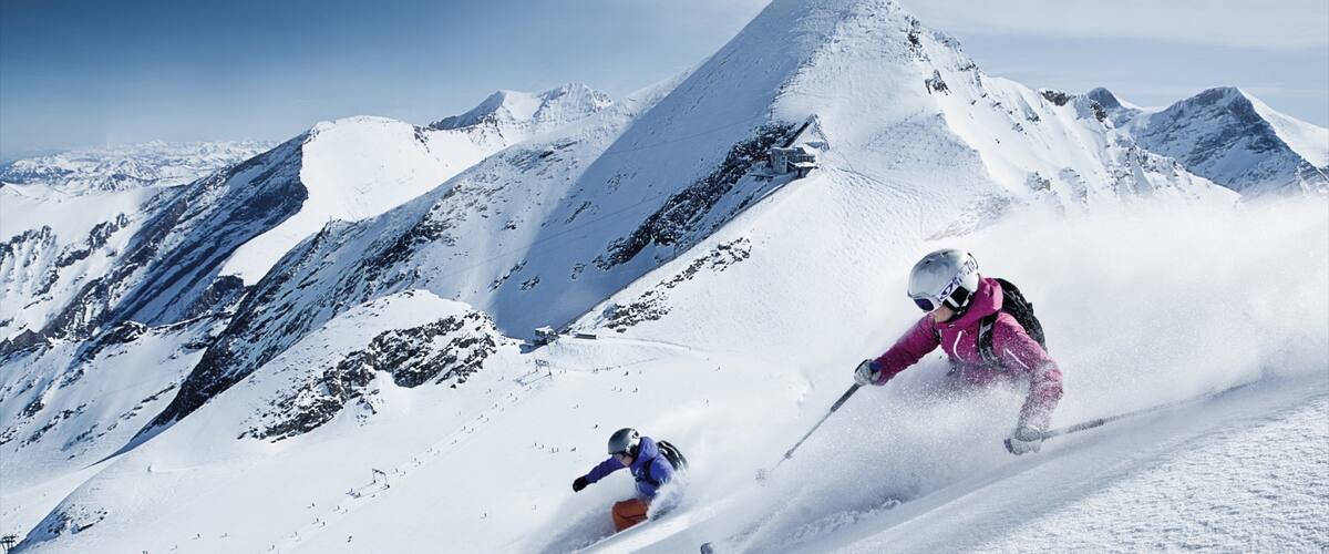 A skier in pink and another in blue skiing down a snowy mountain slope.