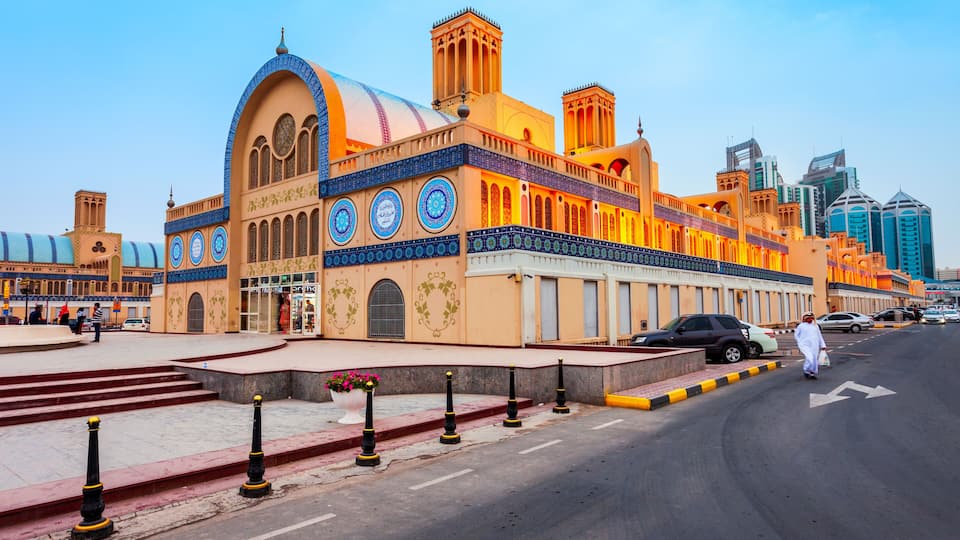 A historic building with ornate blue and gold details, a dome, and a modern cityscape in the background.