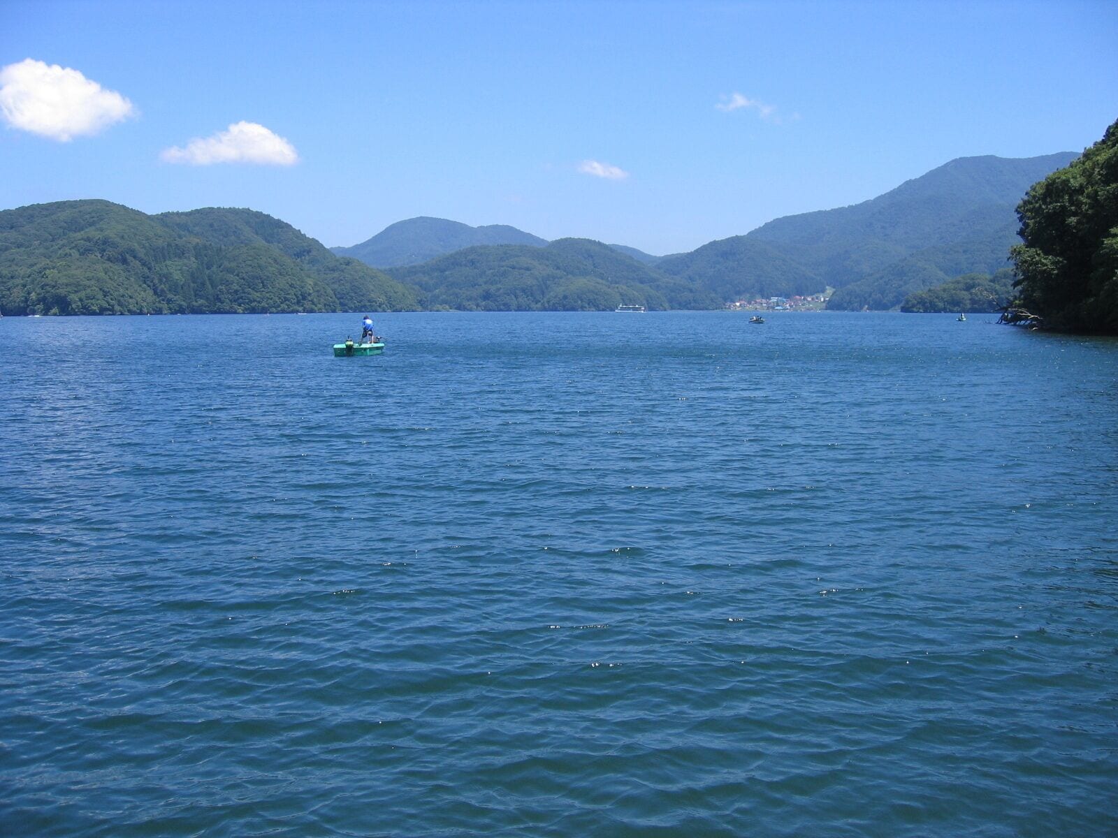 A calm lake with a green boat and a distant shoreline with buildings.