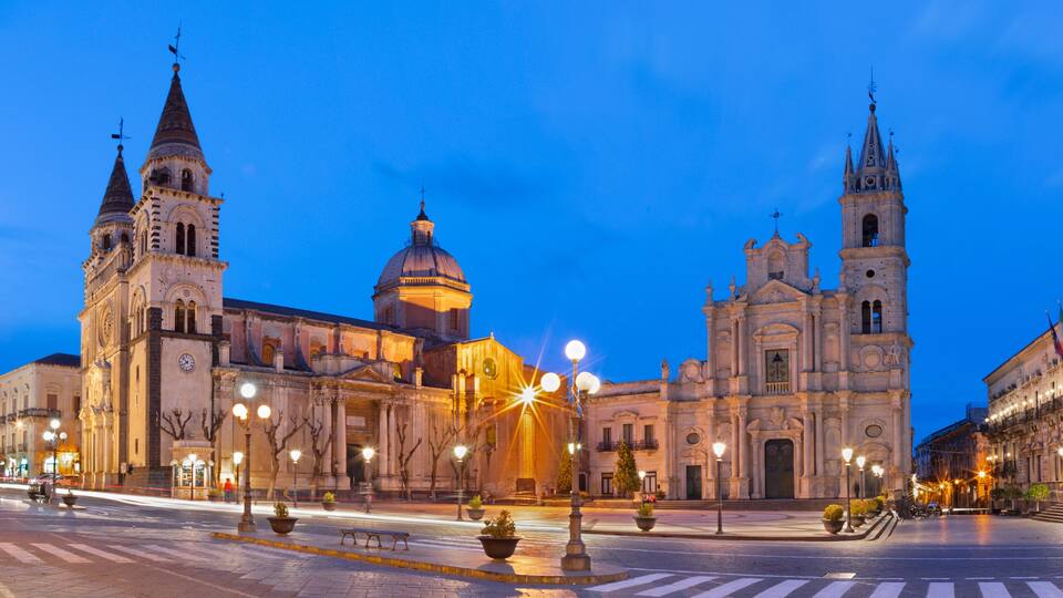 A historic square with ornate buildings, including a church with a dome and twin spires, under twilight sky.