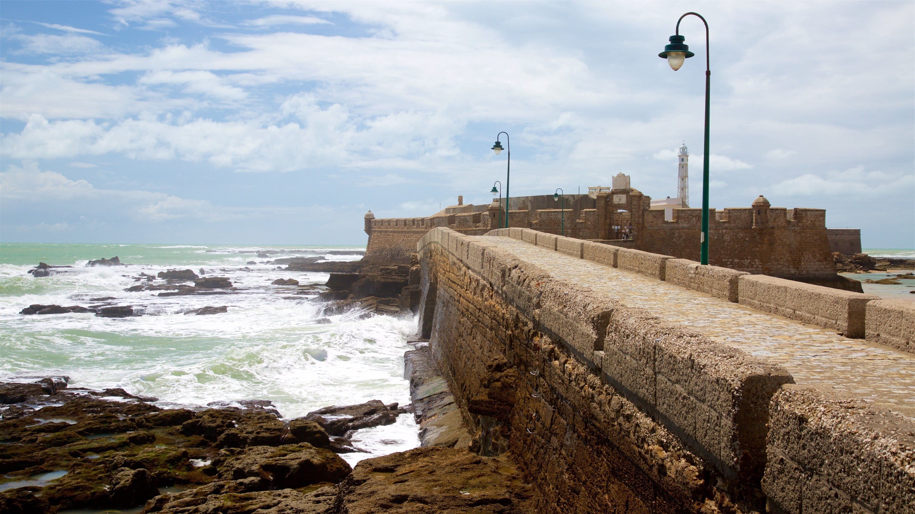A coastal fortification with a stone wall and a lighthouse.