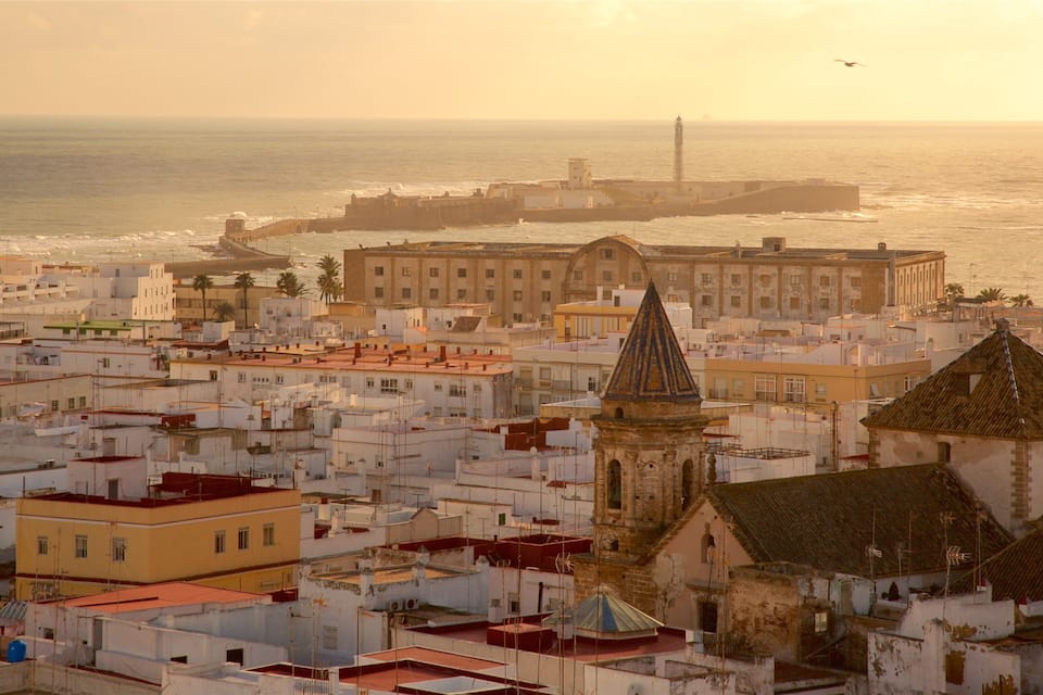 A coastal cityscape with a prominent church tower, a large building with a dome, and a lighthouse in the background.