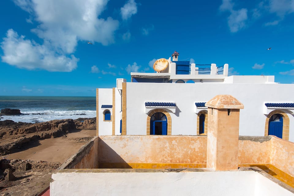 Un edificio costero con puertas y ventanas azules, una antena parabólica y vistas al océano.
