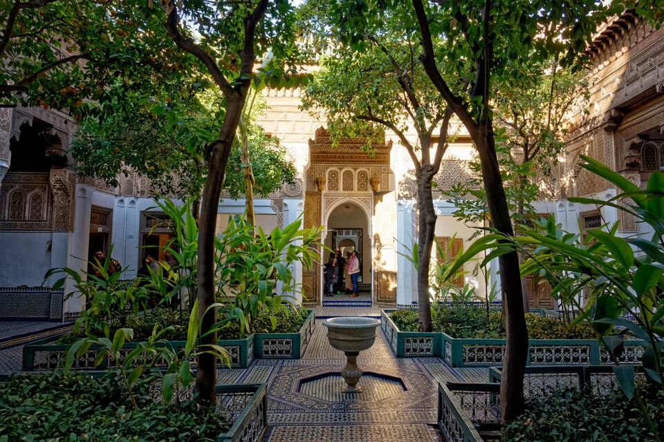 A courtyard with a fountain, surrounded by lush greenery and traditional architecture.