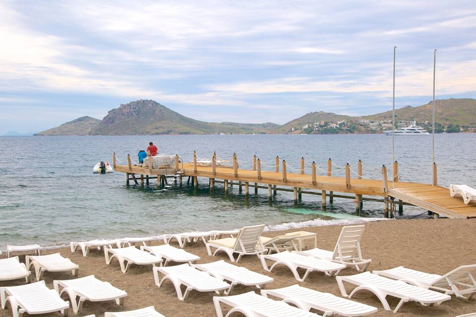 A beach with white lounge chairs and a wooden pier extending into the water.