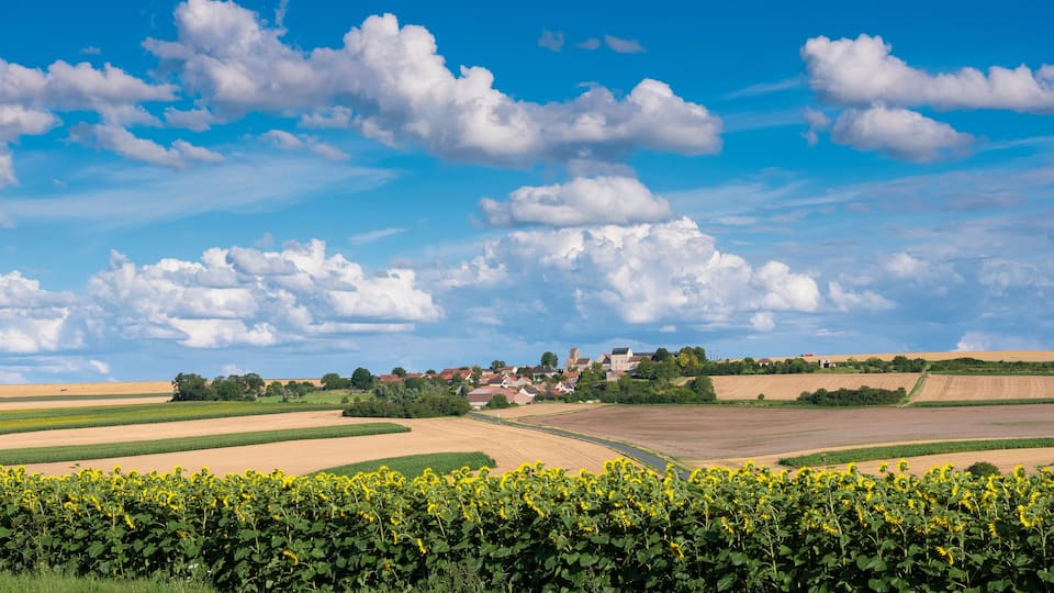 A rural landscape with fields, a village, and a clear sky.