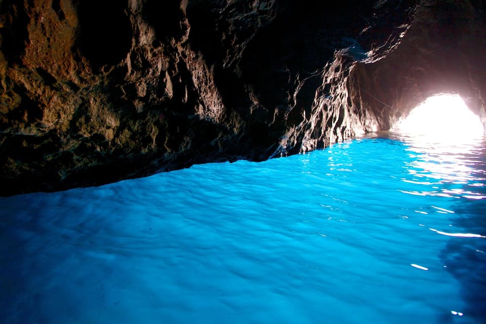 Caverna com luz intensa no fim e água azul cristalina.