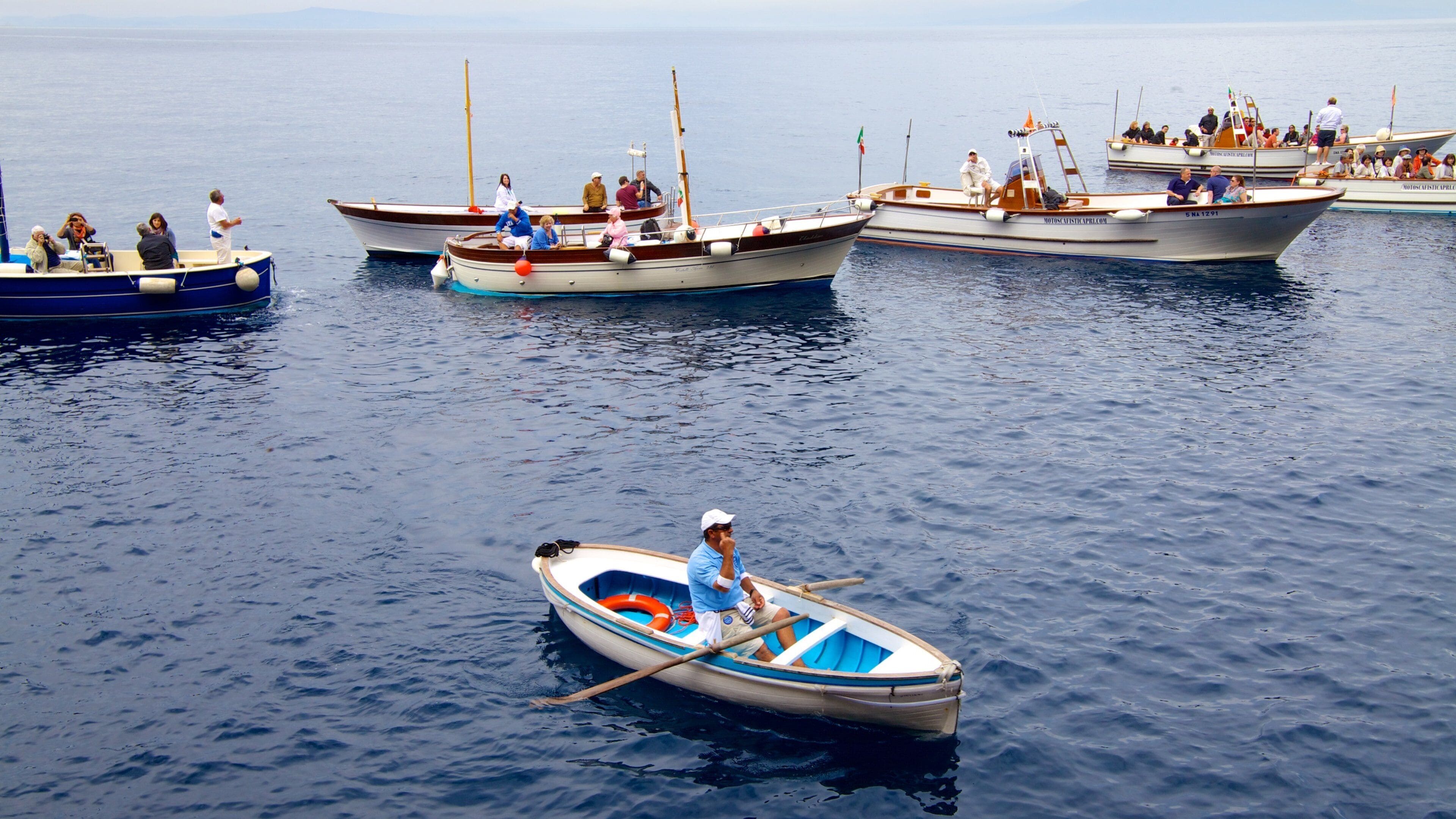 Blue Grotto showing boating and a bay or harbor as well as a large group of people