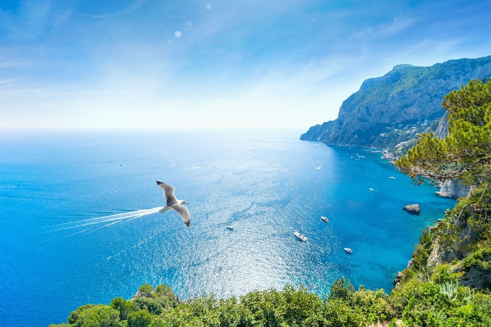 A coastal landscape with cliffs, clear blue sea, and boats.