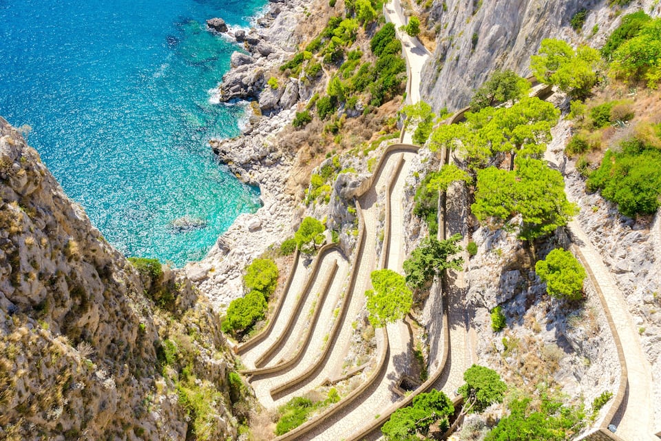 A winding coastal road with a steep cliffside and a clear blue sea.