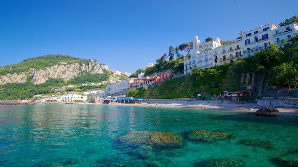 A coastal town with clear turquoise waters, a sandy beach, and buildings on a hillside.