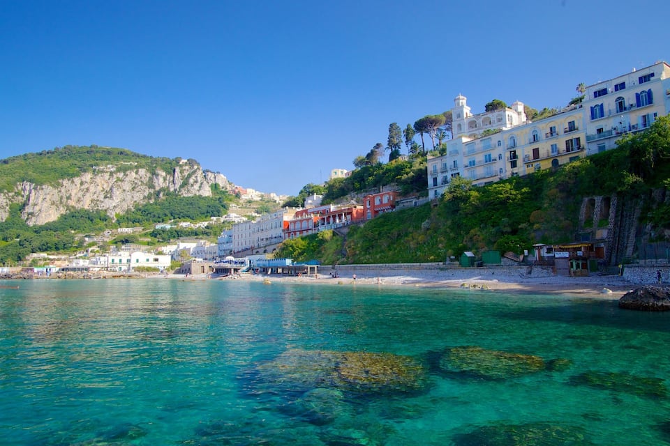 A coastal town with clear turquoise waters, a sandy beach, and buildings on a hillside.