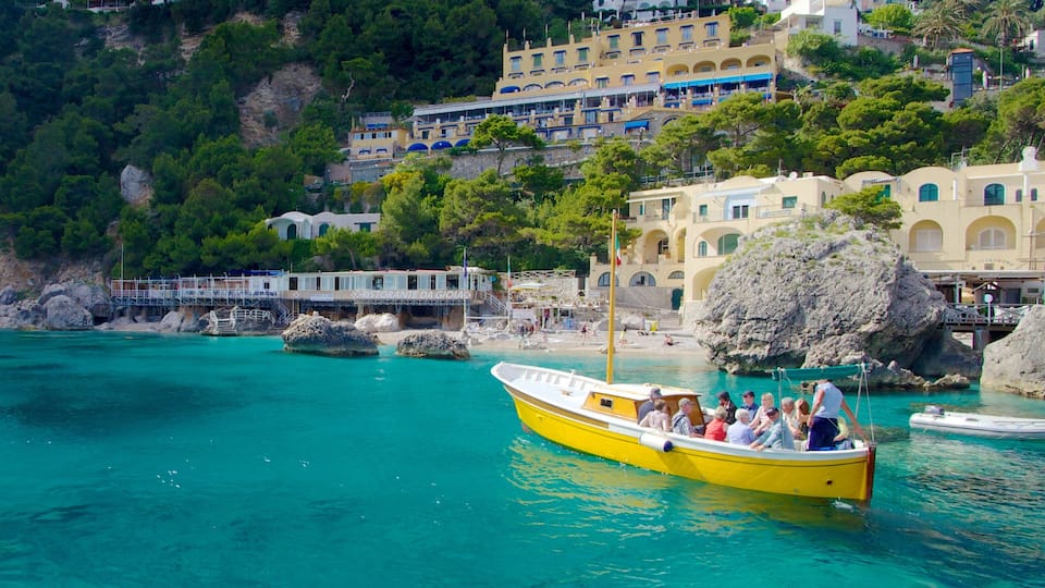A yellow boat with passengers on a turquoise sea, surrounded by rocky shores and buildings with Mediterranean architecture.