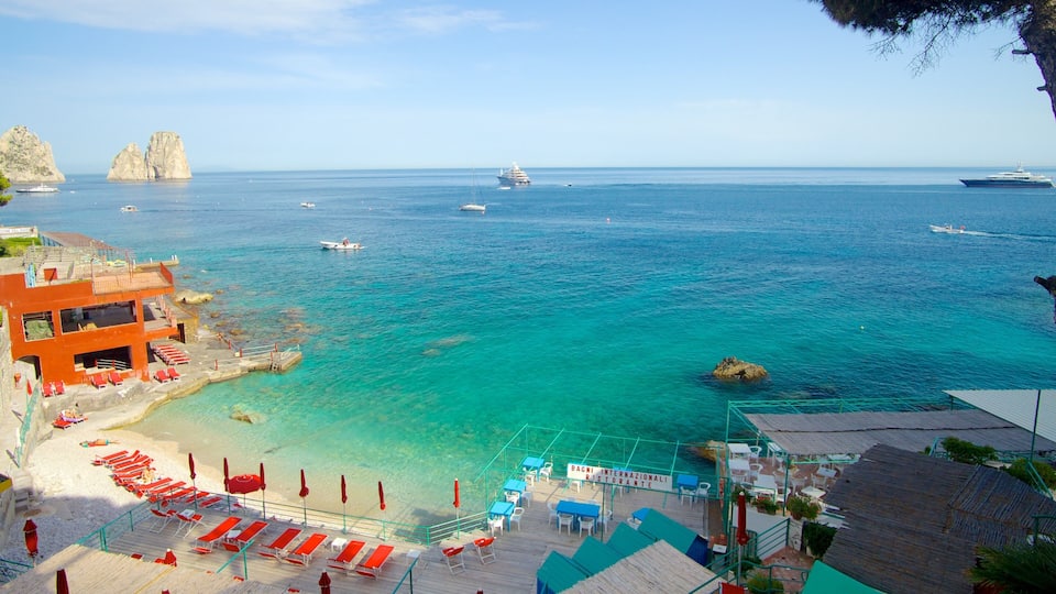 A coastal view with a clear blue sea, a rocky outcrop, and a red building with a terrace.
