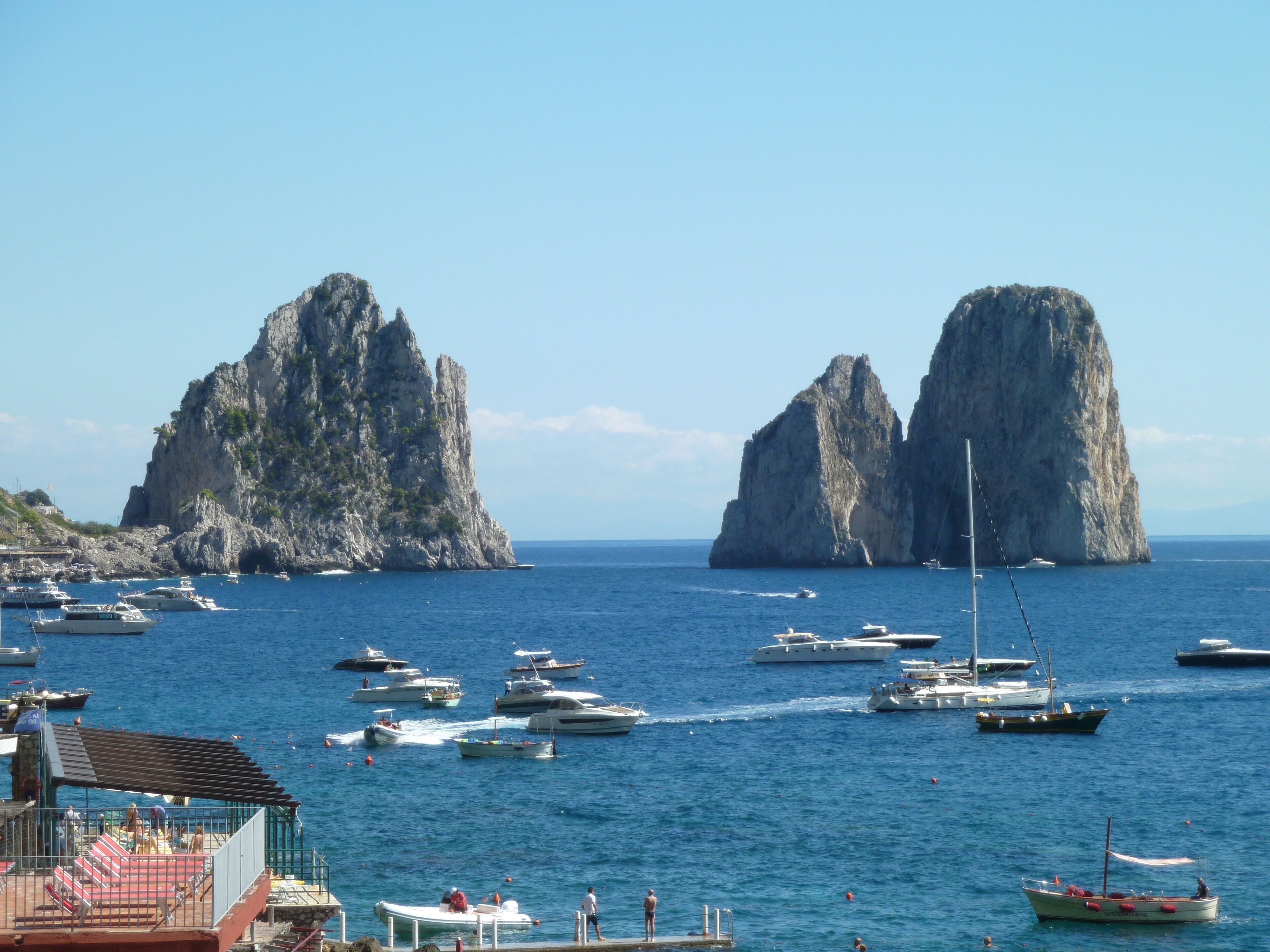 Una marina con barche, scogliere rocciose e un cielo azzurro limpido.