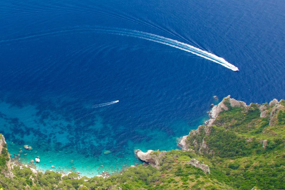 A coastal landscape with clear blue waters, rocky cliffs, and lush greenery.