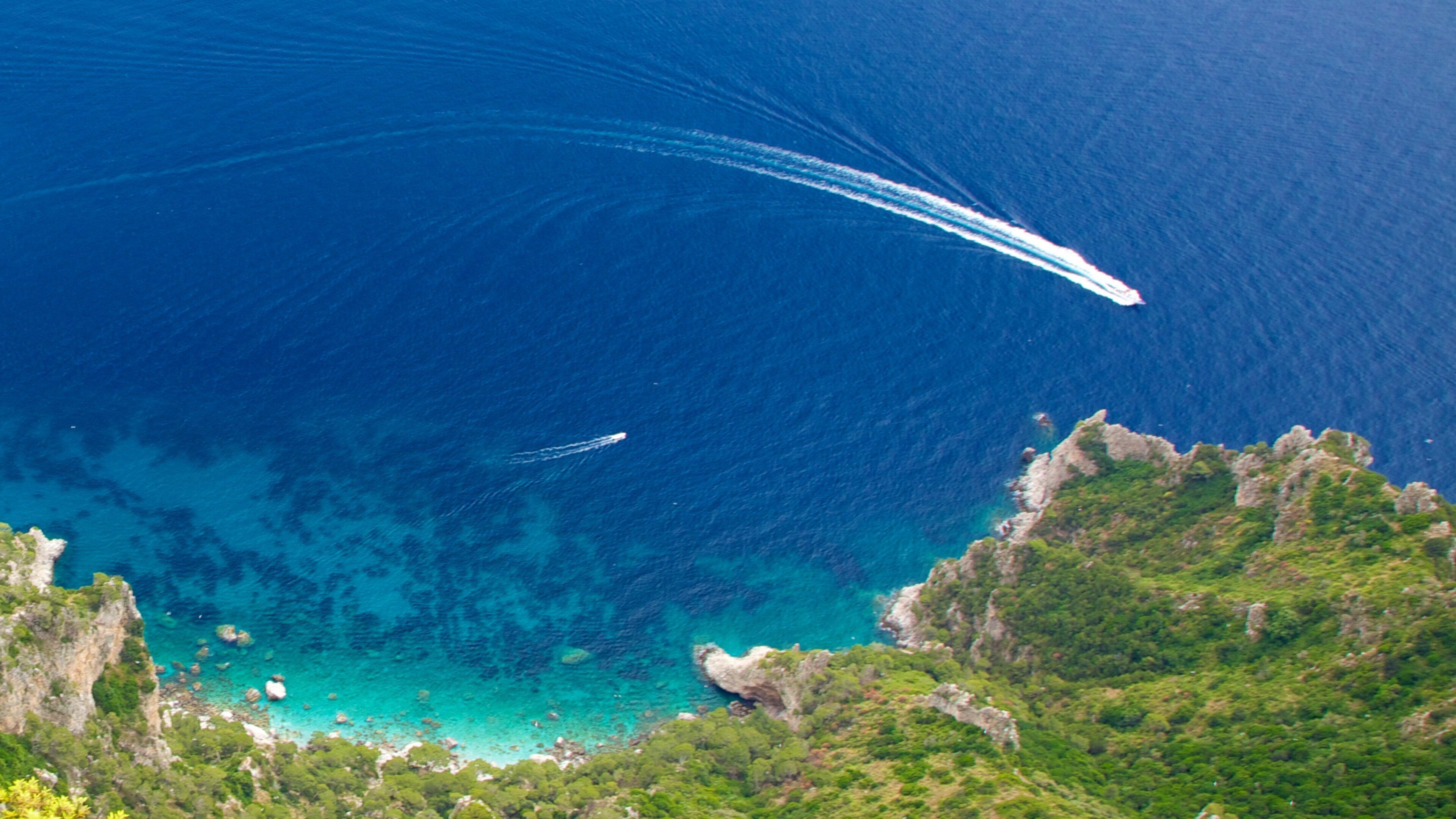 A coastal landscape with clear blue waters, rocky cliffs, and lush greenery.
