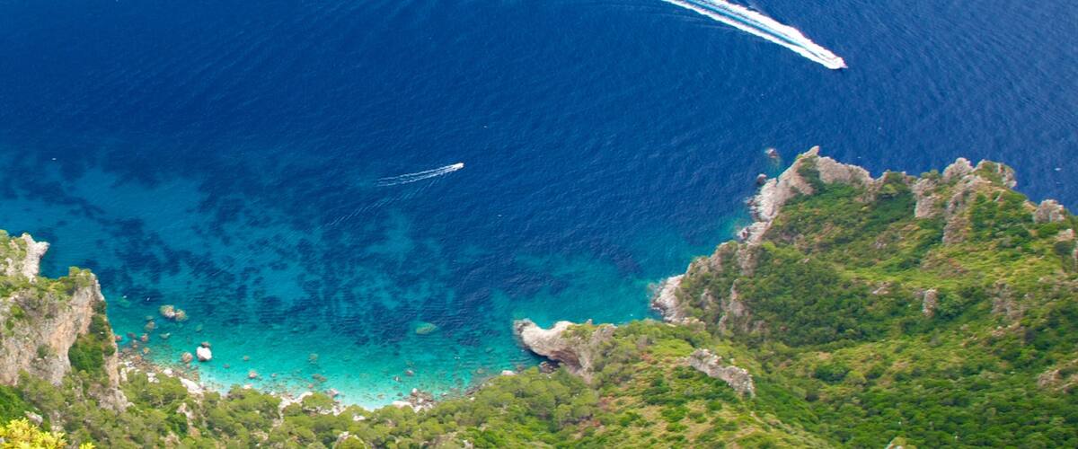 A coastal landscape with clear blue waters, rocky cliffs, and lush greenery.