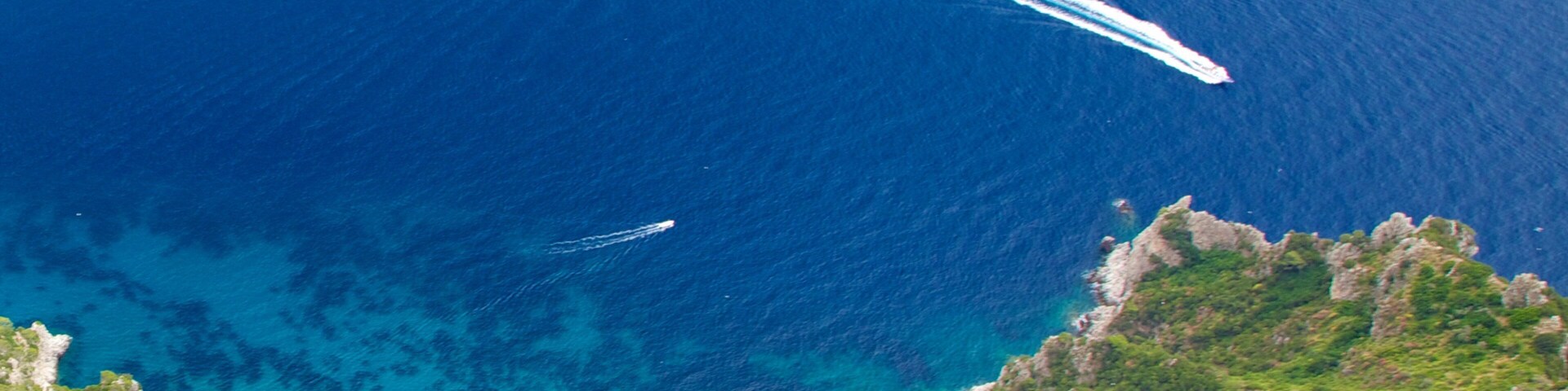 A coastal landscape with clear blue waters, rocky cliffs, and lush greenery.