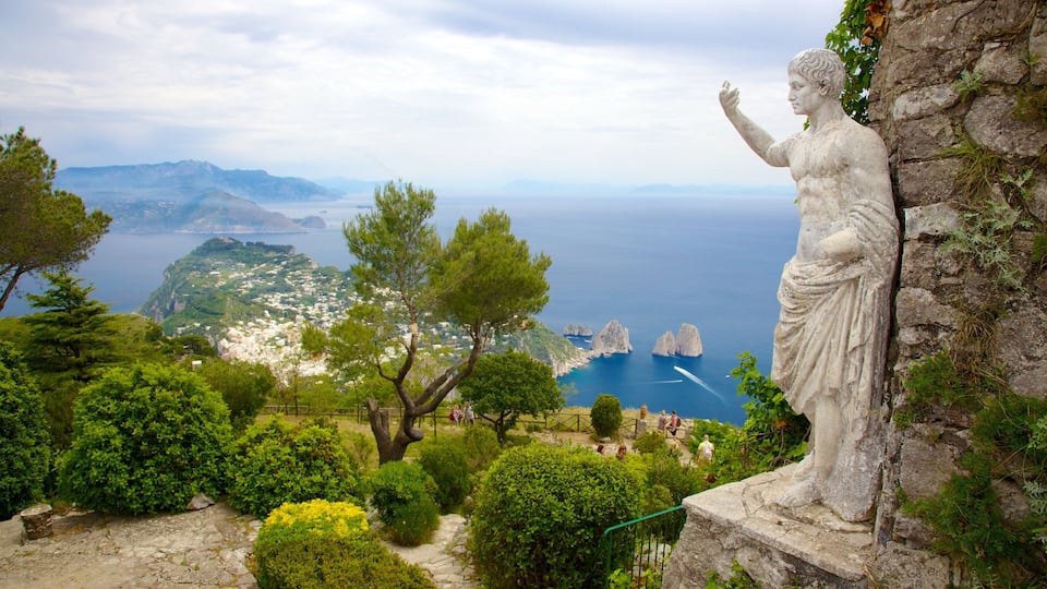 A statue on a cliff overlooking a coastal town with mountains in the background.