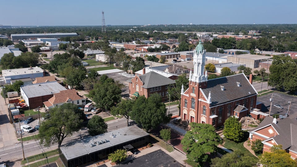 A church with a tall steeple, surrounded by residential buildings and a parking lot.