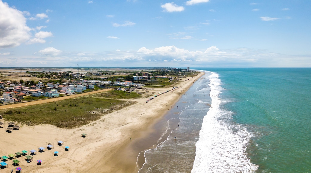 Aerial drone view of the beach, tourists, sea and waves splashing in the coast of the town Playas General Villamil, Ecuador. Sunny day. Beach houses and the horizon with some clouds in background.