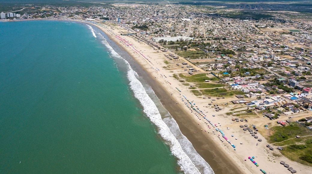 Aerial drone view of the beach, tourists, sea and waves splashing in the coast of the town Playas General Villamil, Ecuador. Sunny day. Beach houses and the horizon with some clouds in background.