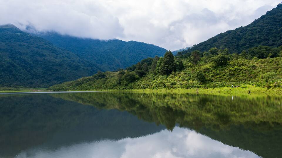 A calm lake reflecting mountains and clouds.