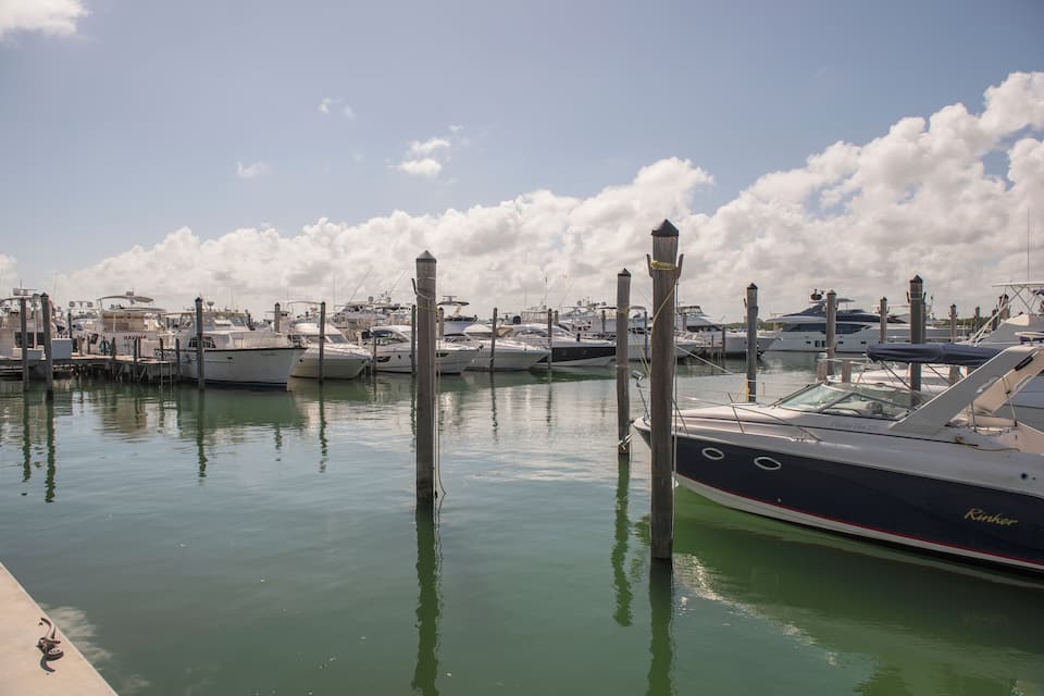 A marina with several boats docked, wooden pilings, and a clear sky with clouds.